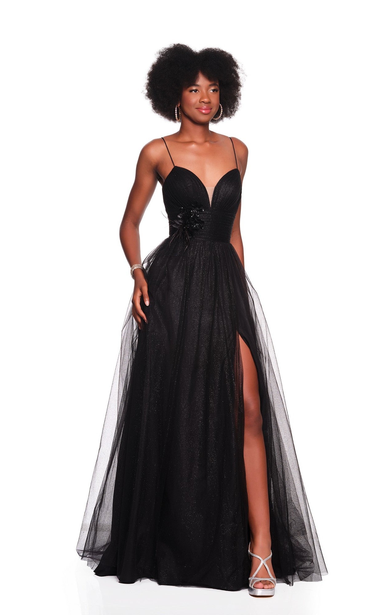 A woman in the Black Glitter Prom Ball Gown: Dave & Johnny 12380, featuring thin straps and a thigh-high slit, poses against a white background in silver heels and hoop earrings—the perfect glamorous look for prom.